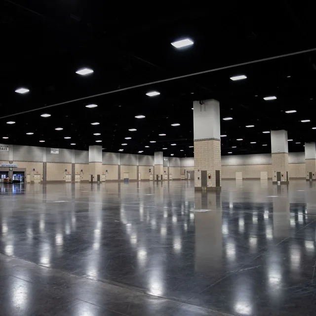 A spacious, empty convention hall with polished floors and numerous overhead lights, featuring beige walls and columns.