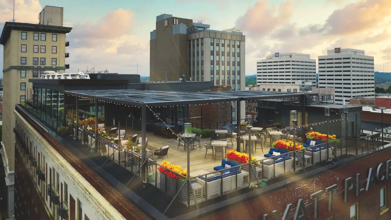 Rooftop terrace of Hyatt Place featuring outdoor seating and vibrant flower planters, with city skyline and cloudy sky in the background.